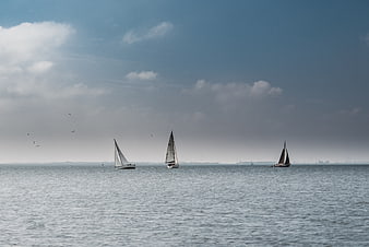 Sailboats on calm sea with blue sky and clouds