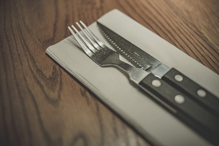 Close-up of silverware on napkin over wooden table
