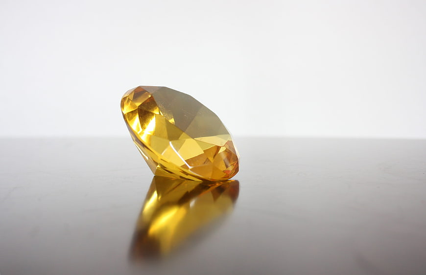 Faceted yellow gemstone on reflective white surface