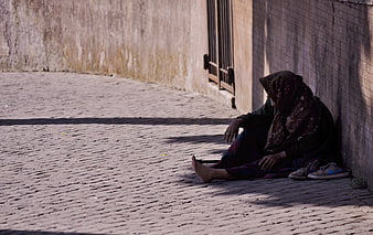 Elderly woman sitting alone on cobblestone street