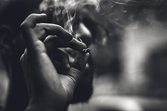 Close-up of hand holding lit cigarette with smoke