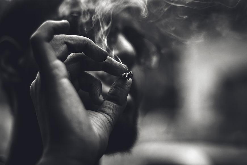 Close-up of hand holding lit cigarette with smoke