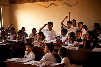 Indian school children raising hands in classroom