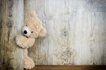 Cute beige teddy bear peeking from rustic wooden wall corner