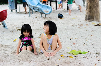 Two young girls playing and laughing in the sand at a beach playground