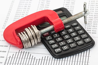 Red clamp squeezing coins on calculator for budgeting