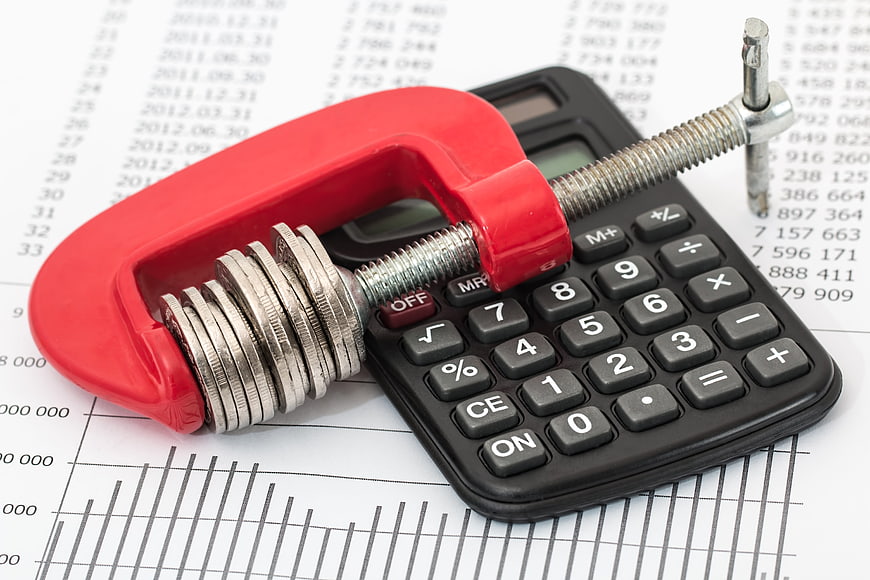 Red clamp squeezing coins on calculator for budgeting