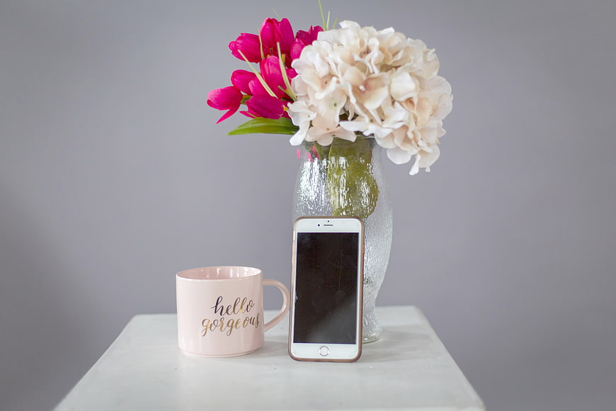 Pink Mug and Smartphone with Flowers on White Table