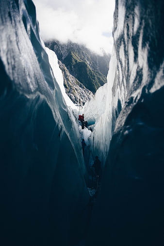 Hikers navigating a deep blue glacial crevasse canyon