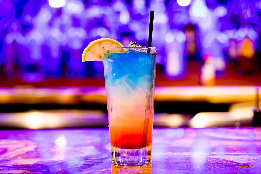 Colorful layered cocktail with lemon garnish on bar counter