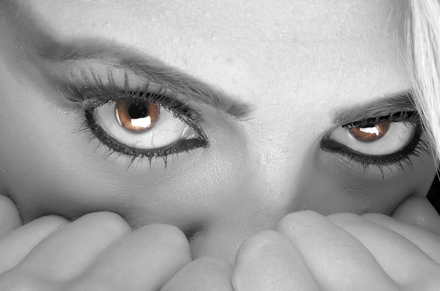 Close-up of woman's eyes with selective color and hands covering mouth