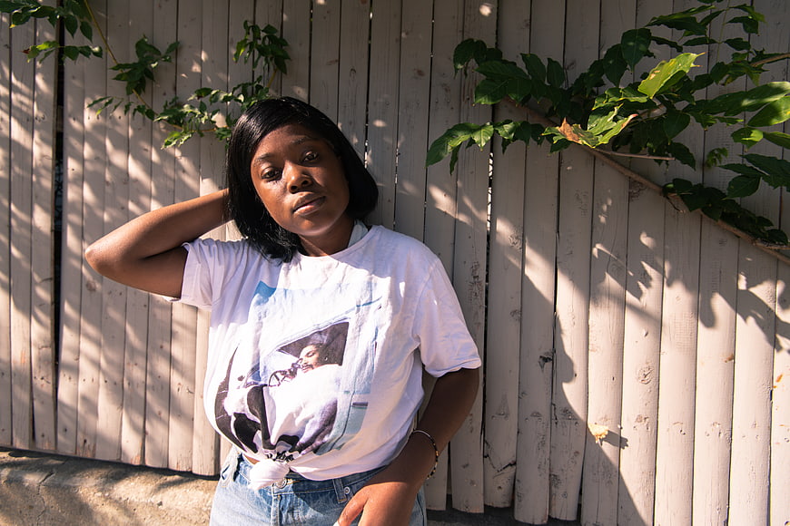 Young Black Woman in Graphic Tee Against Wooden Fence