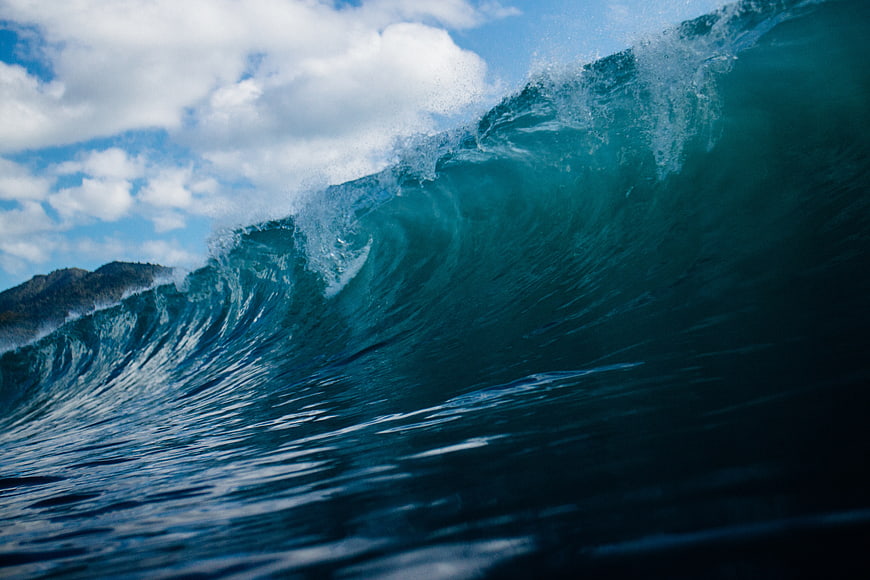 Powerful turquoise ocean wave crashing against a mountain backdrop