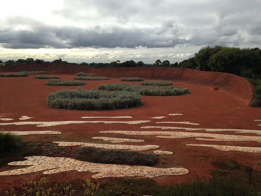 Red earth landscape with stone pathways and shrubs under cloudy sky