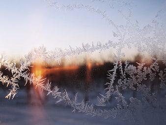 Frost patterns on window glass with blurred winter sunset background