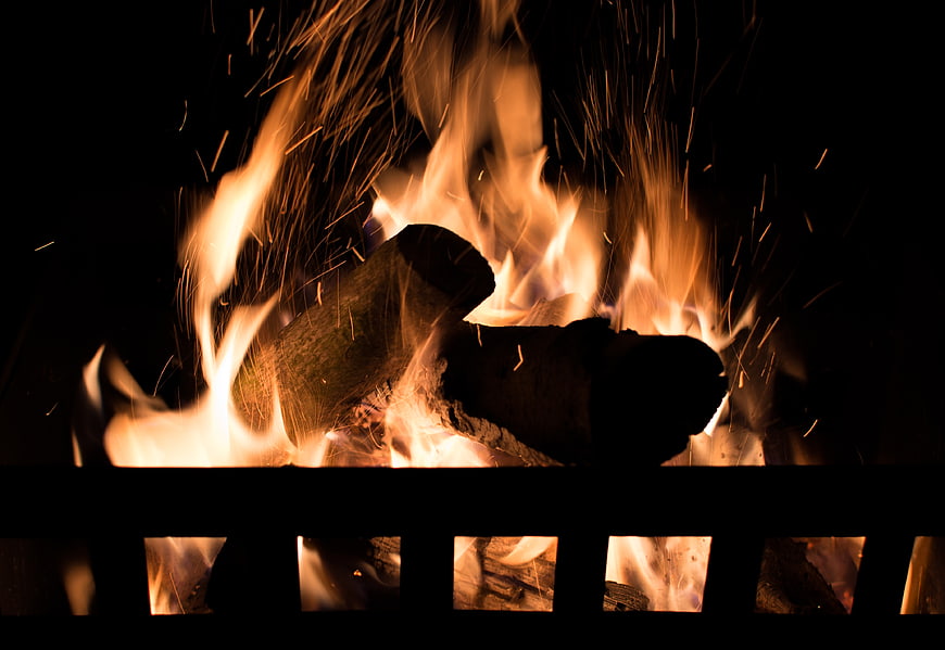 Close-up of burning logs and sparks in a fire pit at night