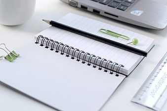 Spiral Notebook, Black Pencil, and Green Clips on White Desk