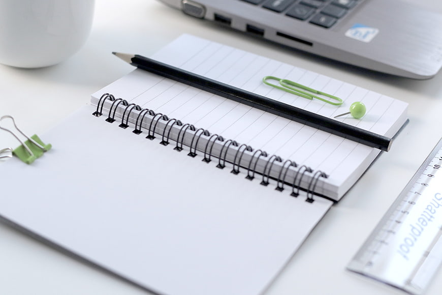 Spiral Notebook, Black Pencil, and Green Clips on White Desk