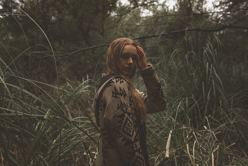 Woman in Patterned Hoodie Standing in Tall Forest Grass