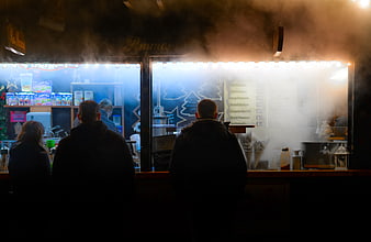 Silhouettes of people ordering at a steamy food stall at night