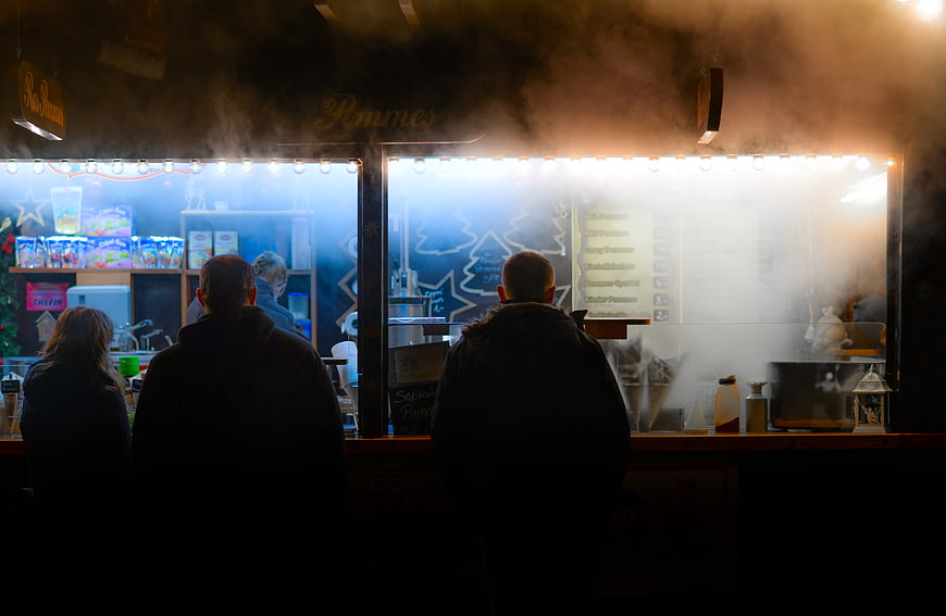 Silhouettes of people ordering at a steamy food stall at night