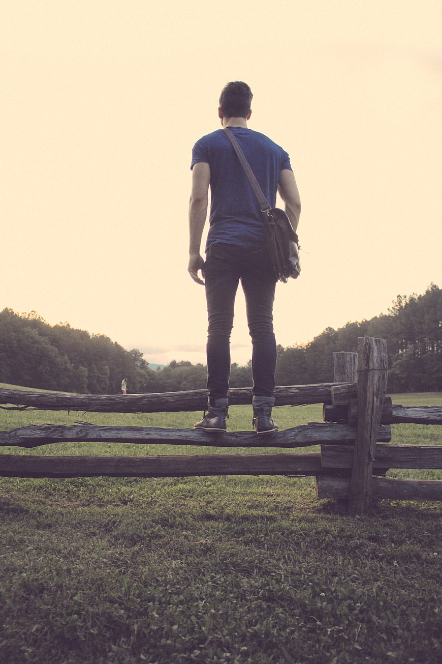 Man standing on wooden fence looking at sunset landscape