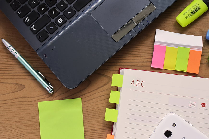 Flat lay of laptop, notebook, and office supplies on wooden desk