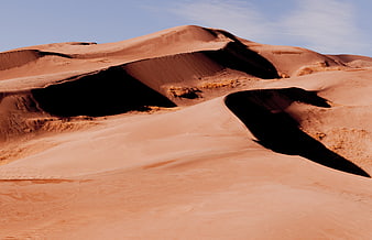 Red sand dunes with deep shadows under blue sky