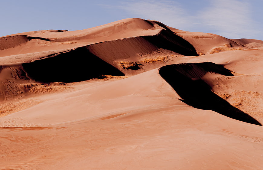 Red sand dunes with deep shadows under blue sky