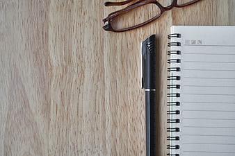 Minimalist workspace with notebook, pen, and glasses on wood
