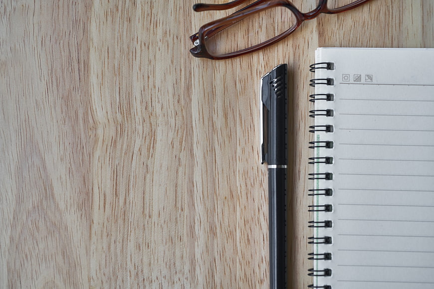 Minimalist workspace with notebook, pen, and glasses on wood