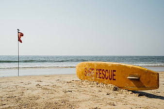 Yellow Surf Rescue Board on Sandy Beach with Red Flag
