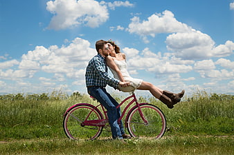 Romantic couple kissing on pink bicycle in summer meadow