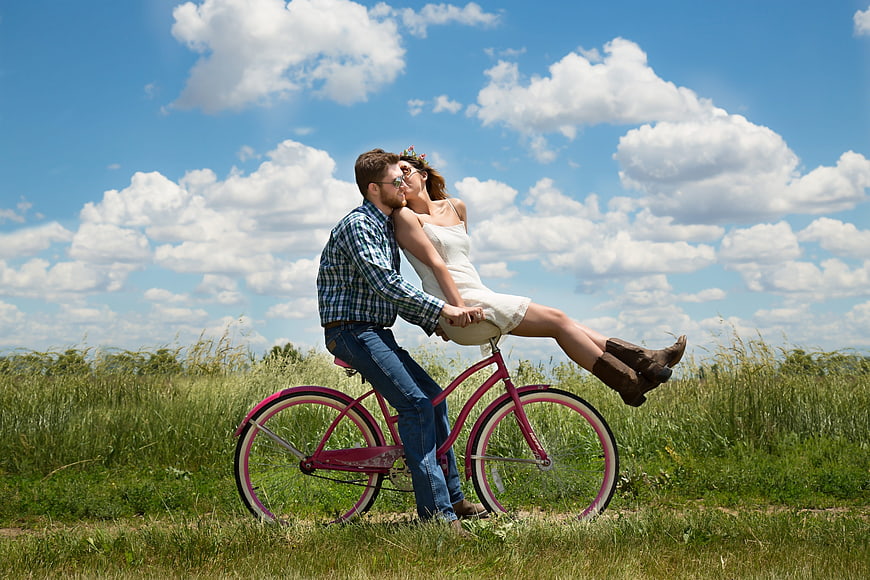 Romantic couple kissing on pink bicycle in summer meadow