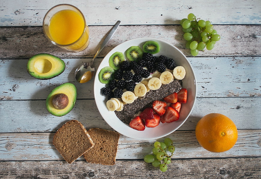 Healthy Breakfast Flat Lay With Fruit Bowl, Avocado, Bread, And Orange Juice