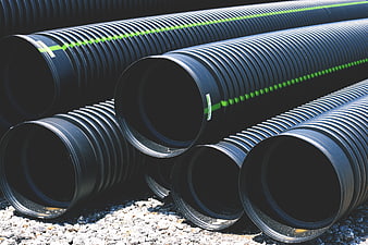 Stacked Black Corrugated Pipes with Green Stripes on Gravel