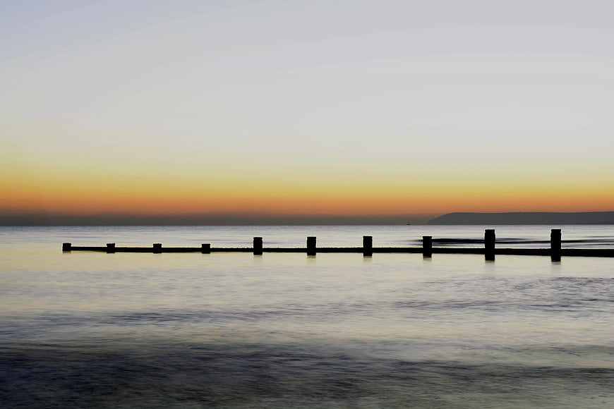 Silhouetted Pier at Sunset Over Calm Ocean Water