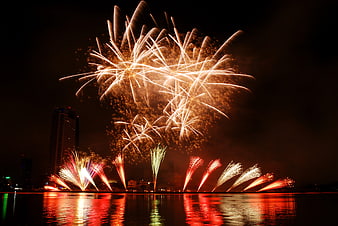 Spectacular golden fireworks exploding over city waterfront at night