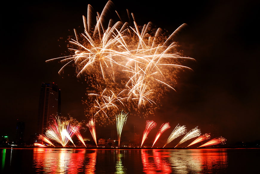 Spectacular golden fireworks exploding over city waterfront at night