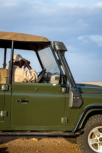Safari guide using binoculars in green jeep