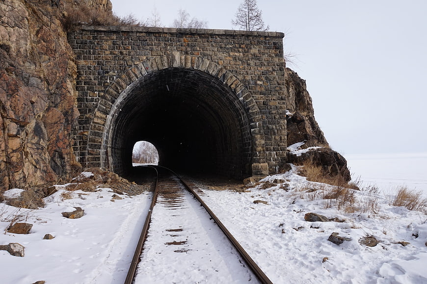 Snowy railway tracks leading into a stone tunnel entrance in winter