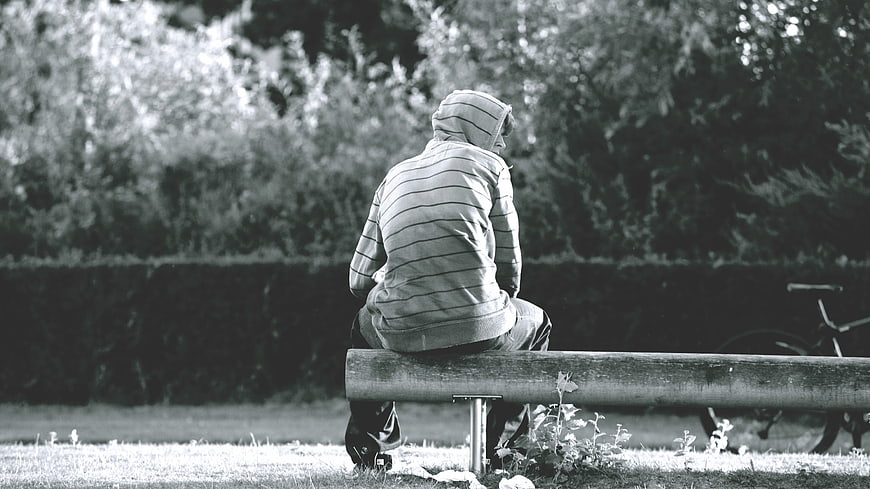 Lone figure in hoodie sitting on park bench