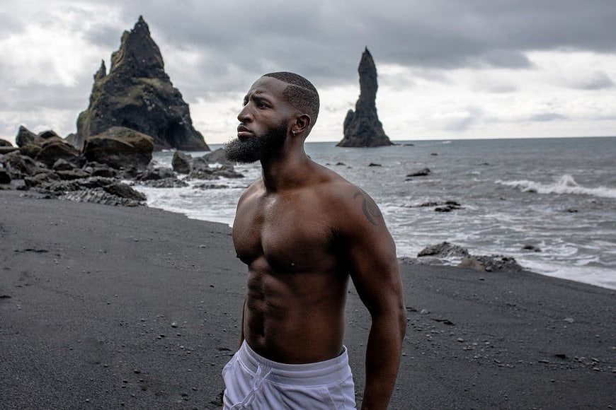 Shirtless Black Man Standing on Black Sand Beach