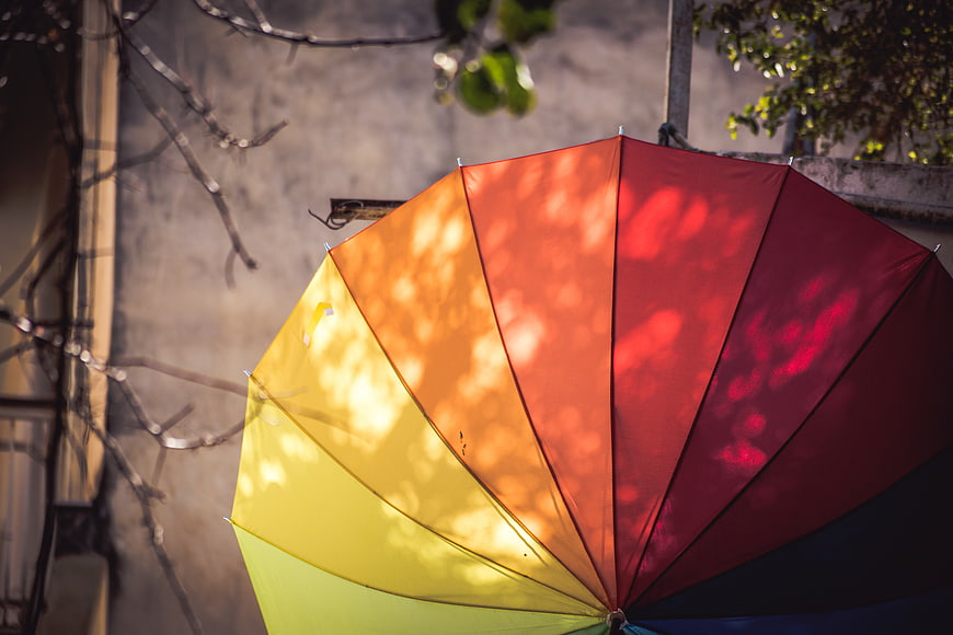 Colorful rainbow umbrella with dappled sunlight shadows