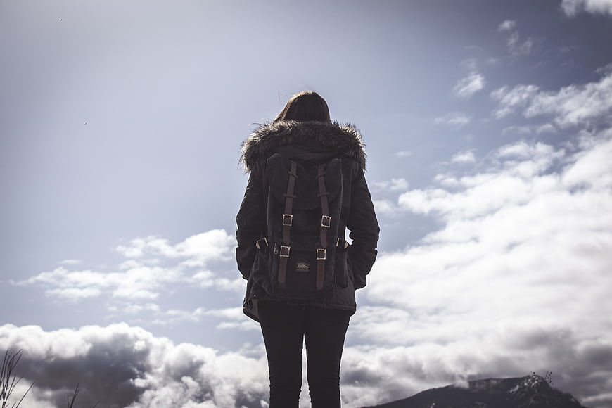 Woman with Backpack Standing Against Cloudy Mountain Sky