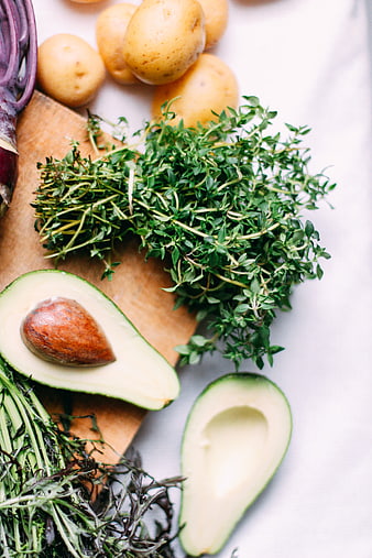 Fresh thyme, avocado, and potatoes on wooden board