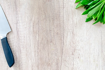 Kitchen knife and fresh green leaves on light wooden table background