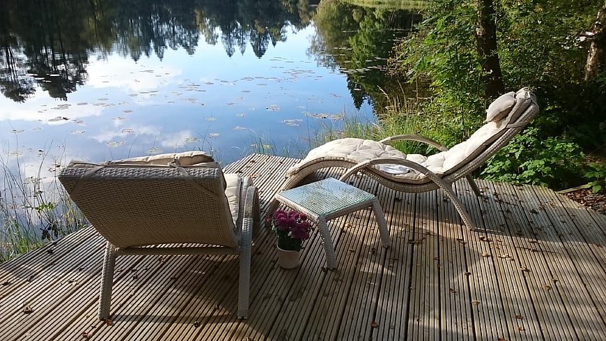 Relaxing wicker lounge chairs on wooden deck by lake