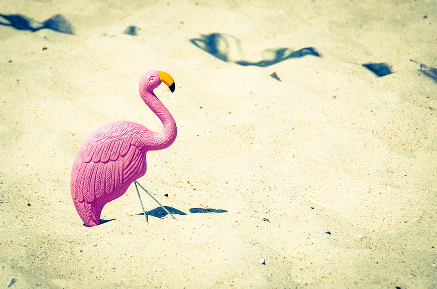 Pink flamingo lawn ornament on sandy beach