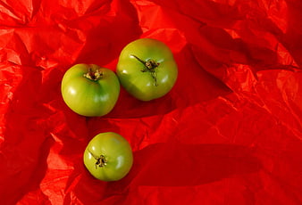 Three Green Tomatoes on Crumpled Red Paper Background